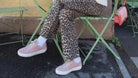Woman sitting at an outdoor cafe table with a pink drink, wearing leopard print pants and sunglasses.